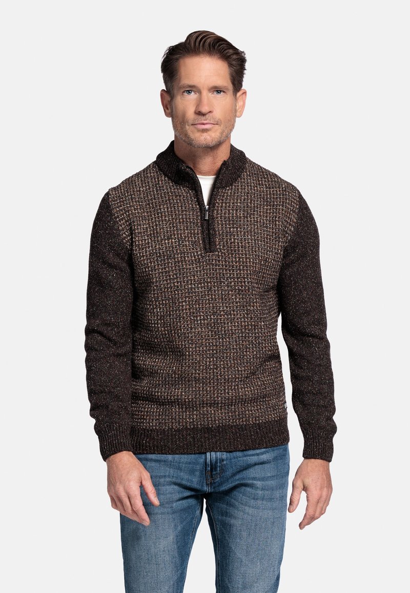 Bruine en zwarte gebreide trui met een ritssluiting kraag, textuurpatroon en geribde manchetten, gecombineerd met lichtblauwe jeans.