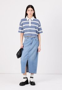 Camisa polo listrada em azul e branco com gola, combinada com uma saia de denim de fenda alta e sapatos plataforma pretos de sola grossa.