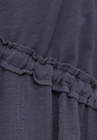 Un tissu gris foncé présente une surface douce et texturée avec un accent froncé le long de la couture, mettant en valeur son design en couches.