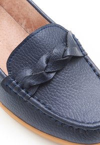 Mocassino in pelle blu scuro con accento intrecciato, superficie texture e suola beige. Presenta dettagli cuciti lungo i bordi superiori.