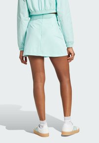 Woman wearing light blue short skirt, matching cropped jacket, white socks, and white sneakers with light blue stripes, standing facing away.