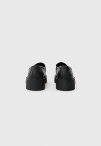 Scarpe in pelle nera con punta arrotondata e superficie liscia. Suola in gomma nera spessa e dettagli di cucitura minimi sul tallone.