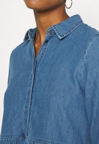 Ljusblå denimskjorta med knapp-up design, krage och rynkade sömmar vid midjan, med strukturerad tyg.