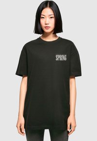 Sort bomulds T-shirt med korte ærmer, der har teksten "Tropical SPRING" i hvid på fronten, rund halsudskæring og afslappet pasform.