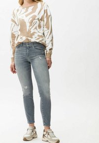 Suéter beige y blanco con estampado y mangas largas, combinado con jeans ajustados de color azul claro con detalles desgastados y zapatillas beige.