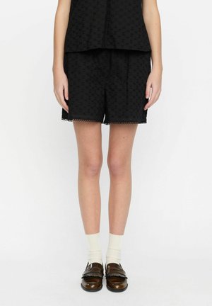 Svarta shorts i texturerad tyg med blommönster, med en scalloped nederkant. Matchas med bruna loafers och krämfärgade strumpor.