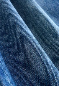 Tejido de denim en un azul profundo con un sutil tejido en sarga. Presenta una ligera textura con costuras visibles y variaciones de color. Superficie lisa.