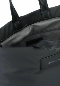 Bolsa tote negra con un exterior suave, asas de cuero y un interior gris con un bolsillo con cremallera. Etiqueta de la marca visible en el interior.