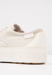 Baskets en toile beige avec semelle blanche épaisse et texturée, petite étiquette de marque sur le côté et col rembourré, vues de l'arrière sur le côté.
