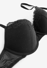 Schwarzer Spitzen-BH mit Netzstoff und floraler Spitzenverzierung an den Cups, mit verstellbaren Trägern, flach auf weißem Hintergrund liegend.
