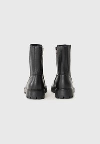 Botas de cuero negras hasta el tobillo con un acabado texturizado, cremalleras laterales y suelas gruesas tipo "lugs", presentando un diseño elegante y minimalista.