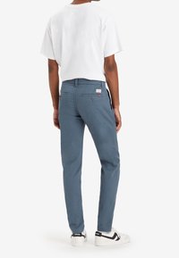 Ljusblå bomullbyxor med smal passform, bakfickor och en logopatch. Bärs med en vit t-shirt och vita sneakers.