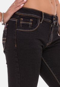 Zwarte denim jeans hebben contrasterende oranje stiksels, een vijf-pocket ontwerp en een slim fit. Inclusief decoratieve hardware en textuurstof.