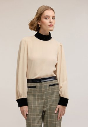 Beżowa bluzka z długim rękawem z czarnym aksamitnym kołnierzykiem, w zestawie z spodniami w kratę o wysokim stanie z czarnym skórzanym paskiem i kieszeniami.