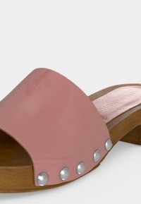 Sandale en bois à bout ouvert avec une bride en cuir rose et cinq clous en argent sur le côté.