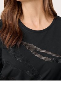 T-shirt nera con scollatura rotonda e un design di strass metallici di diverse dimensioni che creano un motivo su tutta la stoffa.
