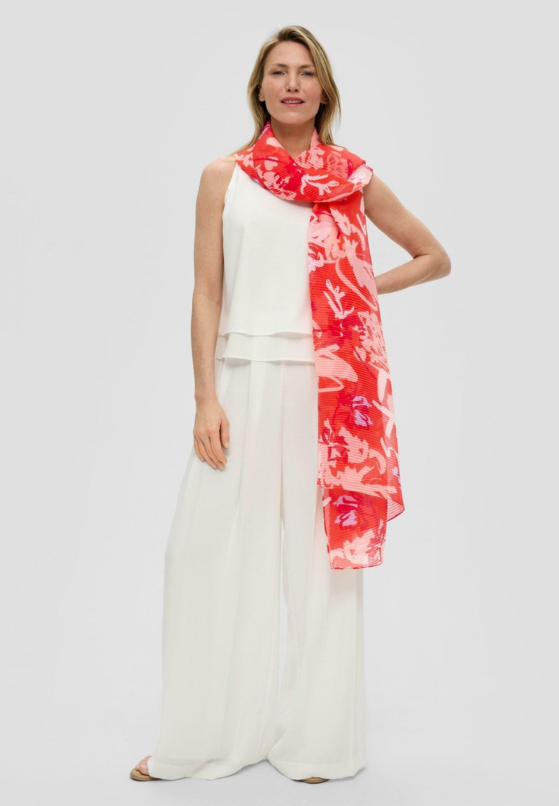 Écharpe florale rouge vive drapée sur un modèle, associée à un haut à couches blanc et un pantalon à jambes larges. Tissu léger et transparent, design vibrant.