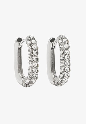 Srebrne kolczyki w kształcie obręczy z rzędem przezroczystych cyrkonii osadzonych po jednej stronie, zaprojektowane z gładkim, polerowanym wykończeniem. Lekkie i o zaokrąglonym kształcie.