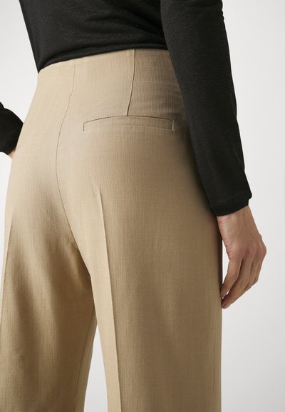 Beige wijde broek van gestructureerde stof, met één achterzak en een hoge taille. Gedragen met een zwart langemouwen top.