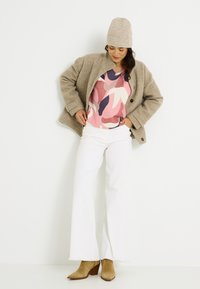 Abrigo texturizado beige, suéter de rayas rosa, jeans acampanados blancos y botines de tacón color beige. Completado con un gorro de punto ligero.