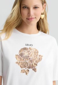 T-shirt bianco con una grafica di rosa a stampa leopardo con accenti scintillanti, completata dal nome del marchio "LIU·JO" sopra il design.