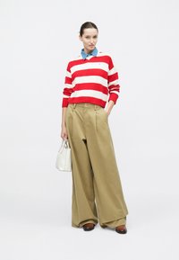 Κόκκινο και λευκό ριγε πουλόβερ φορεμένο πάνω από ένα τζιν πουκάμισο με γιακά, συνδυασμένο με ψηλόμεσα, φαρδιά χακί παντελόνια και καφέ παπούτσια.