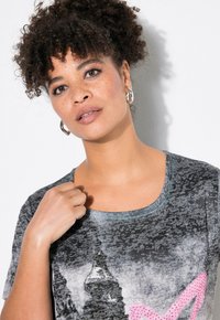 Camiseta gráfica con cuello redondo, que presenta un estampado de un horizonte urbano y detalles en rosa. La tela es gris con una apariencia texturada.