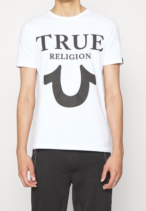 Camiseta de algodón blanca con texto en negrita negro que dice "TRUE RELIGION" y un diseño de herradura invertida. Mangas cortas y un cuello clásico tipo crew.