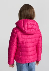 Giacca imbottita rosa con cappuccio, caratterizzata da linee trapuntate orizzontali e polsini elastici, abbinata a jeans in denim. Vista posteriore.