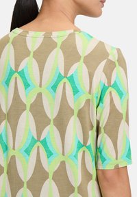 Multicolored patterned top featuring a repeating design of ovals and diamonds in shades of green and aqua on a beige background.
