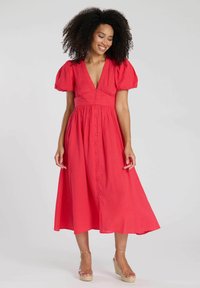 Röd midiklänning med korta puffärmar, djup V-ringning, texturerad tyg och knapprad framtill. Bärs med klara kilklacksandaler.