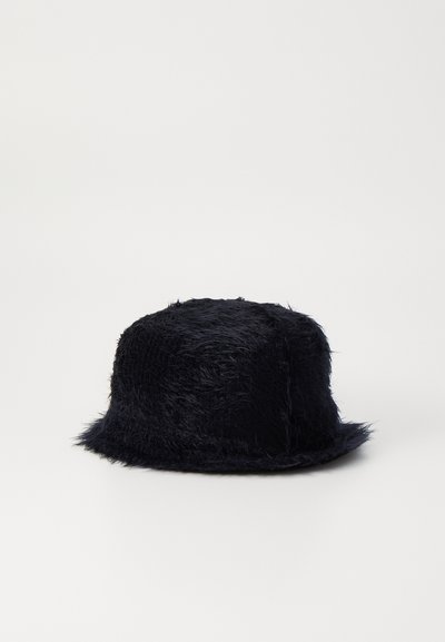 Musthave must-tekin, ümarik lakega, tekstuuriga pind ja veidi laiendatud äärega must faux karvane ämbri müts, millel on pehme ja karvane välimus.