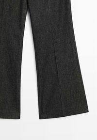 Pantaloni a gamba larga realizzati in tessuto grigio scuro con una leggera lucentezza. Presentano pieghe frontali e un orlo pulito.