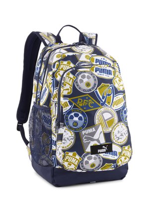 Granatowy plecak Puma z wieloma naszywkami o tematyce sportowej, siateczkową boczną kieszenią, wyściełanymi paskami i przednią kieszenią na zamek.