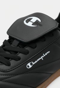 Sneaker din piele sintetică neagră cu sireturi negre plate, limbă căptușită și logo alb "Champion". Prezintă o talpă din cauciuc gumos.