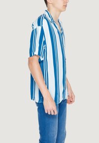 Camicetta a maniche corte con bottoni, a righe verticali blu e bianche, con una vestibilità comoda e un colletto a punte. Tessuto dalla superficie liscia.