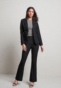 Sort fitted blazer med notch lapels, iført over en grå ribbet top. Parret med sorte flagrende bukser og sorte strop sandaler.