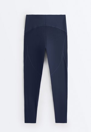 Tamnoplave legice visokog struka pune duljine s zakrivljenim šavovima na bedrima i glatkom, sjajnom teksturom.