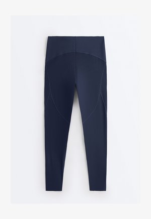 Tamnoplave legice visokog struka pune duljine s zakrivljenim šavovima na bedrima i glatkom, sjajnom teksturom.