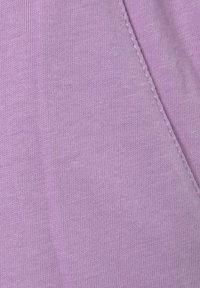 Tissu lilas avec une texture lisse et un motif de tricot fin. Détail de couture visible le long du bord.