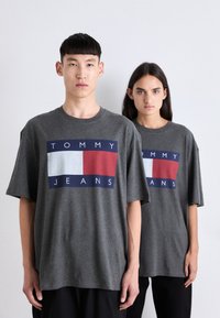 Camisetas de algodón gris con un diseño a bloques de color que presenta acentos en navy, blanco y rojo. Corte relajado y mangas cortas, mostradas en dos modelos.