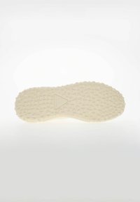 Podeszwa jasnobeżowego buta z trójkątnym, waflowym wzorem bieżnika i małym trójkątnym logo na środku.