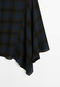 Tissu à carreaux bleu foncé et vert, drapé avec une texture douce ; un ourlet triangulaire aux bords fluides crée une apparence en couches.