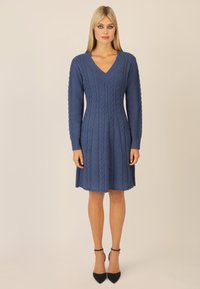 Abito blu a maglia con scollo a V e lunghezza al ginocchio, caratterizzato da un tessuto testurizzato con motivi a cavo in rilievo e maniche lunghe, abbinato a tacchi neri con cinturino alla caviglia.