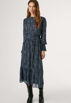 Vestido de manga larga en azul marino con diseño plisado, tela texturizada con rayas metálicas verticales y cintura ceñida. Botas altas negras hasta la rodilla.