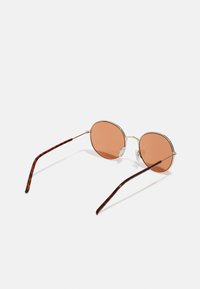 Lunettes de soleil rondes avec des verres roses clairs, monture en métal doré et branches à motif écaille de tortue, dotées de plaquettes de nez ajustables.