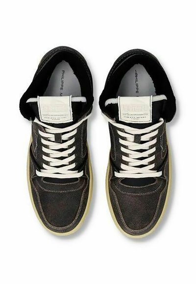 Sneaker in pelle nera con lacci bianchi, dotate di punta rotonda e suola in gomma marrone. La linguetta presenta un'etichetta con logo di forma rettangolare.