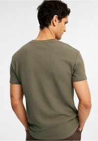 Grøn kortærmet tekstureret t-shirt med et rutenetmønster, rund halsudskæring og afslappet pasform, set fra ryggen.
