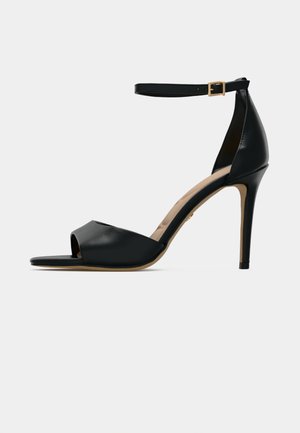 Black high-heeled sandal with open toe, smooth leather upper, ankle strap with gold buckle, and a beige footbed.