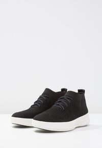Zwarte gebreide hoge sneakers met een textuurpatroon, voorzien van grijze veters en een witte rubberen zool voor contrast.
